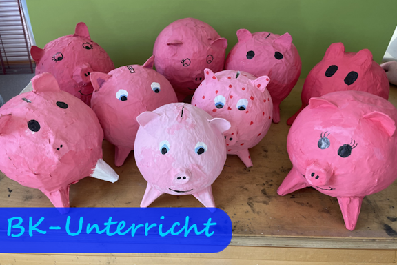 Auf einem Tische stehen mehrere rosa Sparschweine, die aus Papiermaché hergestellt wurden.