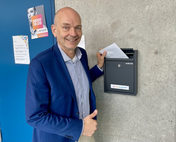 Schulleiter vor dem Briefkasten, wirft Brief ein
