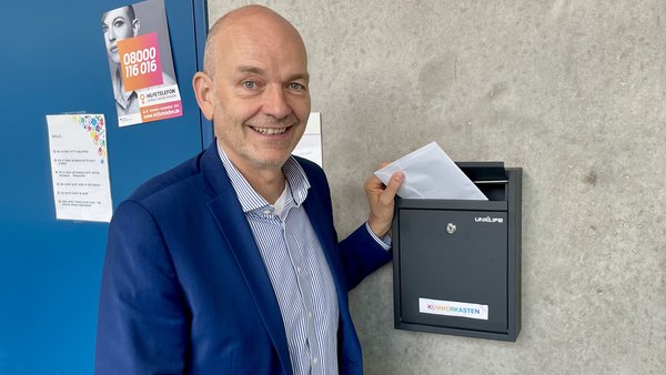 Schulleiter vor dem Briefkasten, wirft Brief ein