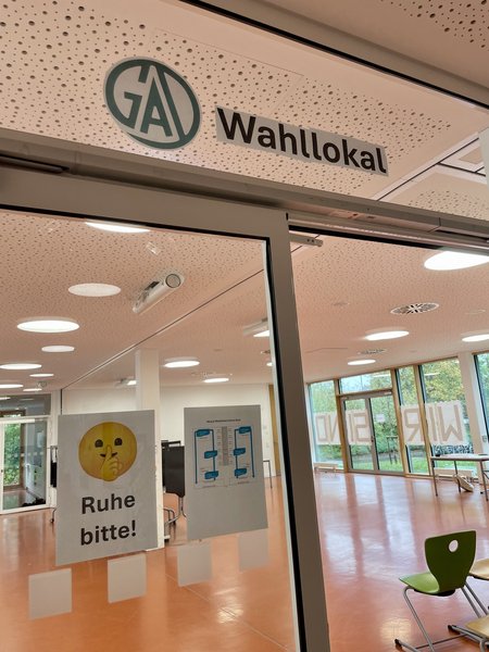 Ein Wahllokal mit einem Schild „Ruhe bitte!“ und einem Plan zur Abstimmungsanleitung an der Tür.